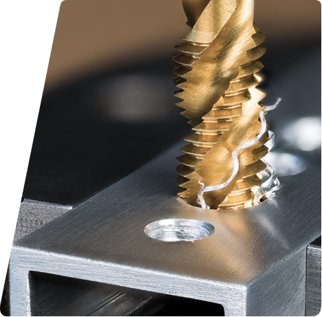 A gold-colored industrial tap cutting threads into a metal workpiece with metal shavings nearby.