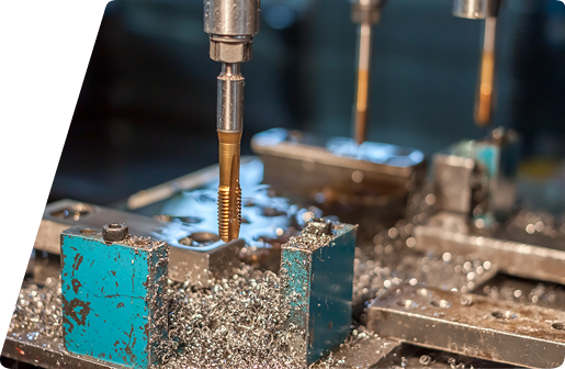 Close-up of a metal tap tool machining a part on a drill press, surrounded by metal shavings.