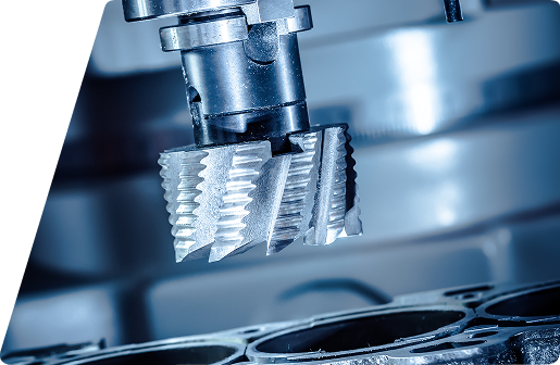 Close-up of a metal milling cutter head positioned over an engine cylinder block in an industrial machining environment.