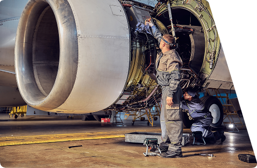 Two mechanics in overalls performing maintenance on a large jet engine inside a hangar.