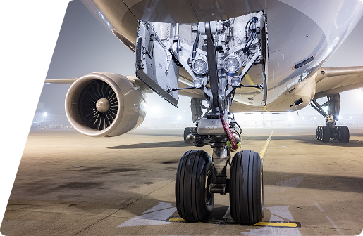 Close-up of an airplane's nose landing gear and jet engine on an airport tarmac at night.