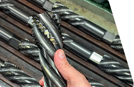Hand holding a metal industrial spiral reamer with similar tools arranged in a rack behind it.
