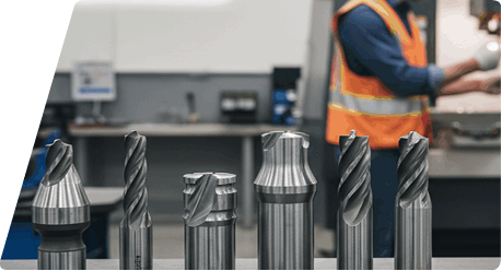 Assorted metal cutting tools lined up on a workbench with a worker in a high-visibility vest in the blurred background.