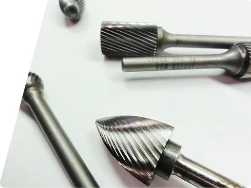 Several metal rotary burr bits with varied tip shapes arranged on a white surface.