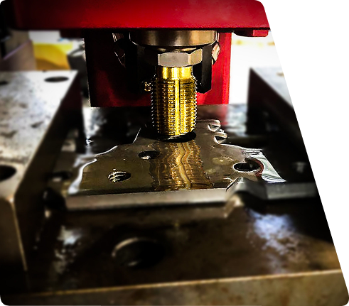 Metal tap tool cutting threads into a lubricated metal part on an industrial machine.